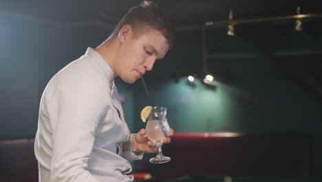 man in white shirt sipping lemon drink with black straw in dimly lit billiard room. relaxed atmosphere with stylish lighting. soft shadows create a moody and sophisticated bar setting