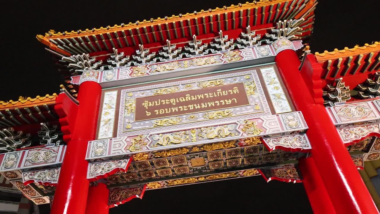 Camera tilts upward on ornate Chinatown archway at night, vibrant lighting, urban background visible