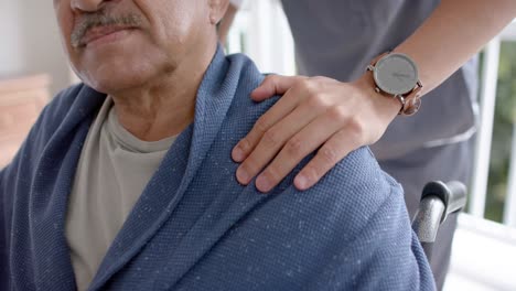 mid section of diverse male doctor and senior male patient in wheelchair at home, slow motion