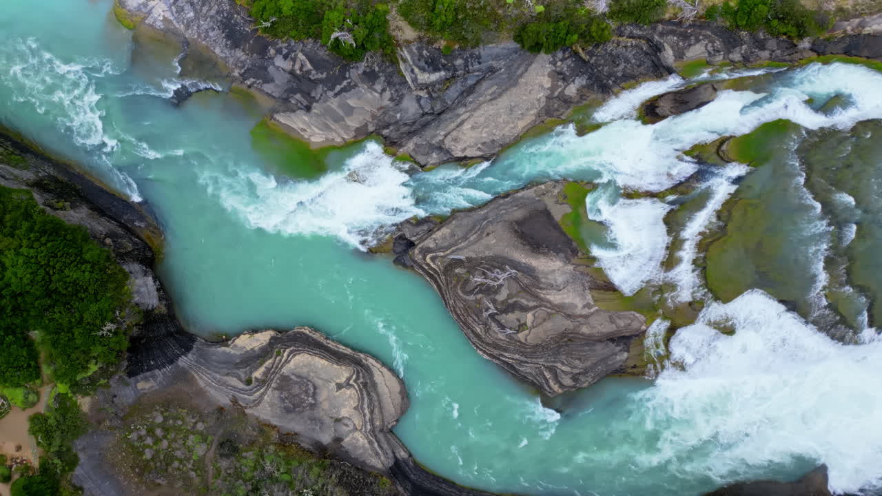 Aerial drone view of fast flowing glacial river cutting through rocky terrain, showing vivid turquoise water and white foam