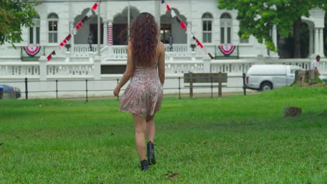 Young-curly-hair-woman-walking-in-a-mini-dress-and-boots-before-turning-around-with-a-castle-in-the-background