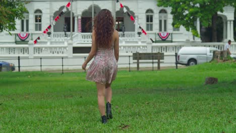 mujer joven de cabello rizado caminando en un mini vestido y botas antes de dar la vuelta con un castillo en el fondo