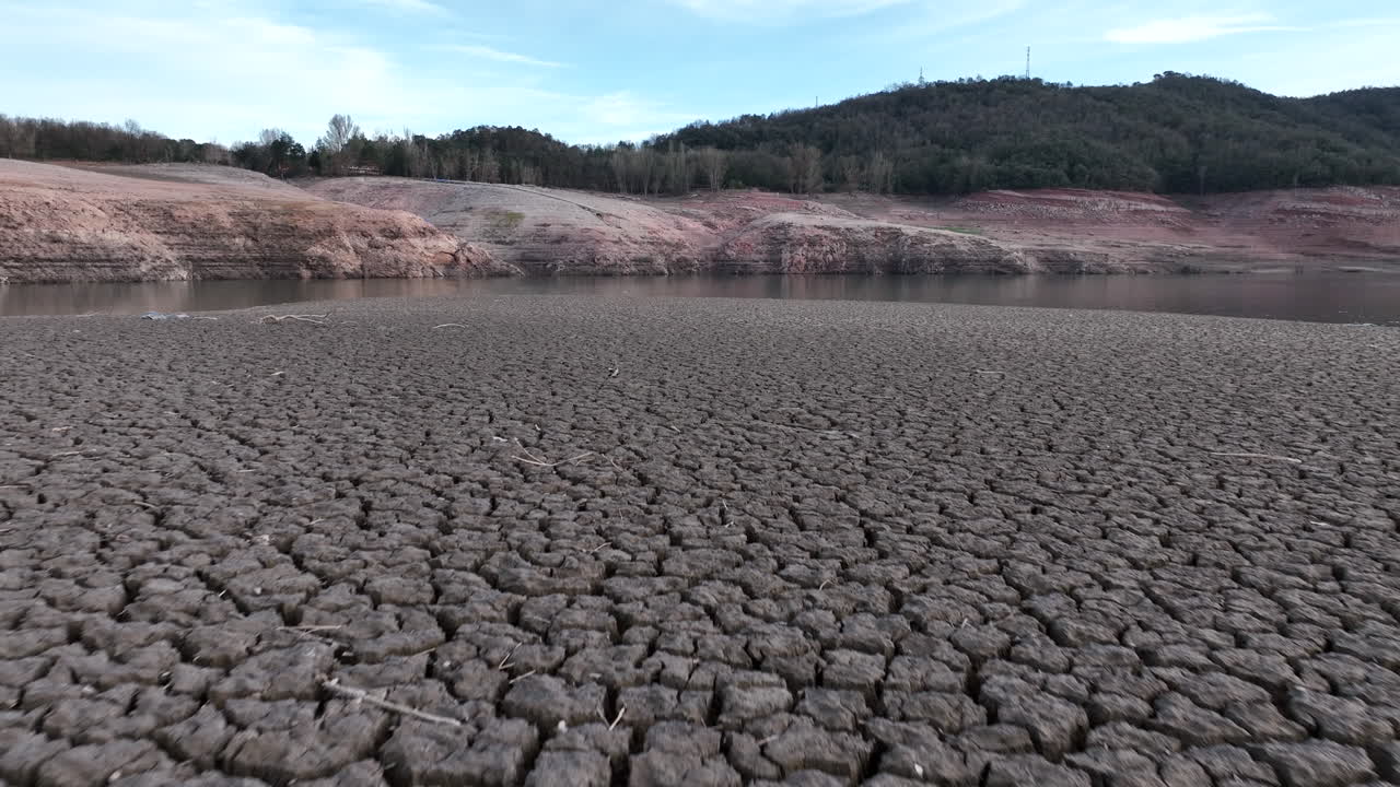 avión no tripulado volando bajo sobre tierra con suelo seco y agrietado lodo seco por la sequía en el pantano de la aldea de sau, cataluña en españa