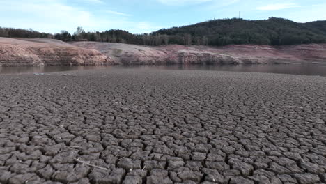 drone flying low over land with dry and cracked muddy dry ground by drought in swamp of sau village, catalonia in spain