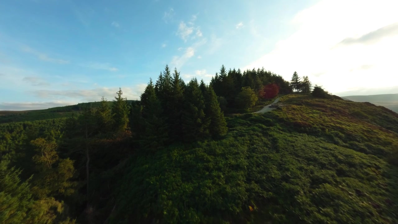Un quadricottero FPV sorvola una collina boscosa di Glendalough mentre il sole basso scintilla sul lago calmo della valle
