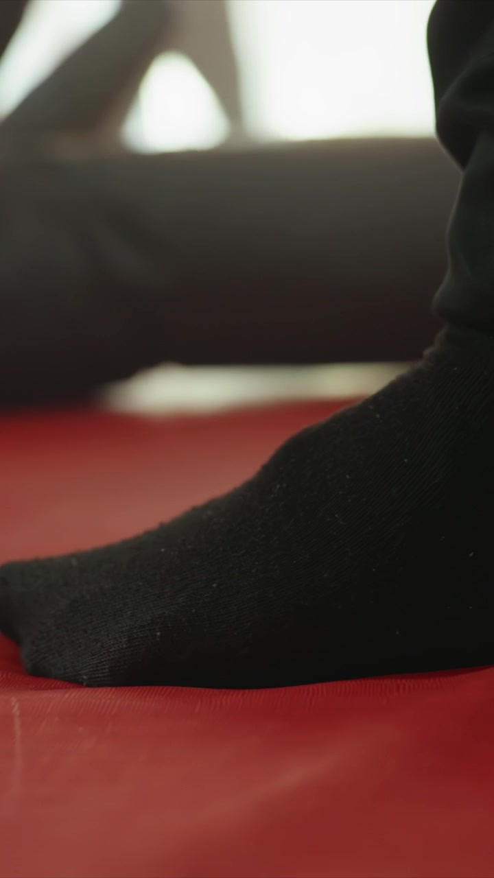 Close up of foot in black sock performing subtle movements. Foot position adjusts slightly suggesting controlled motion. Indoor setting with soft lighting and dark furniture