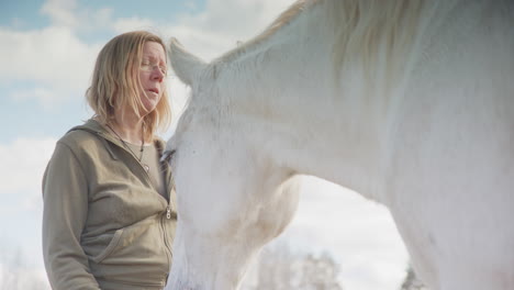 Bond-between-woman-and-white-horse-as-she-kisses-muzzle,-equine-therapy