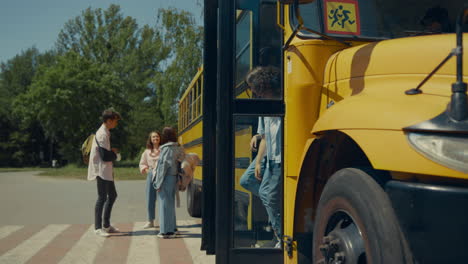 two pupils leaving schoolbus chatting. teenagers standing talking near bus.