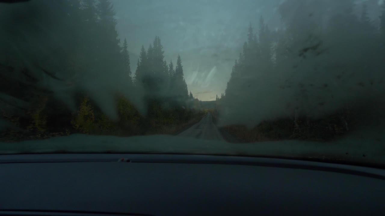 POV Fogged windscreen from a car driving through a dirt road in the middle of a eerie forest at dusk