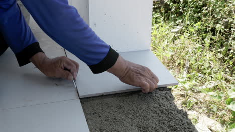 a construction worker puts a tile in place, on top of a freshly mixed mortar then taps it gently using a mallet.