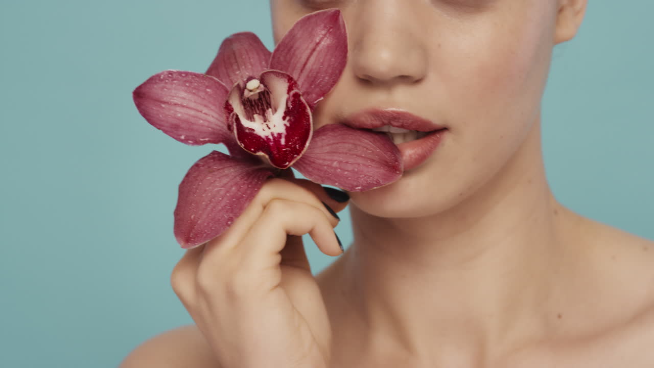 ritratto ravvicinato donna sexy che morde giocosamente fiore d'orchidea che tocca le labbra carnagione perfetta fragranza delicata di essenza naturale concetto sano di cura della pelle