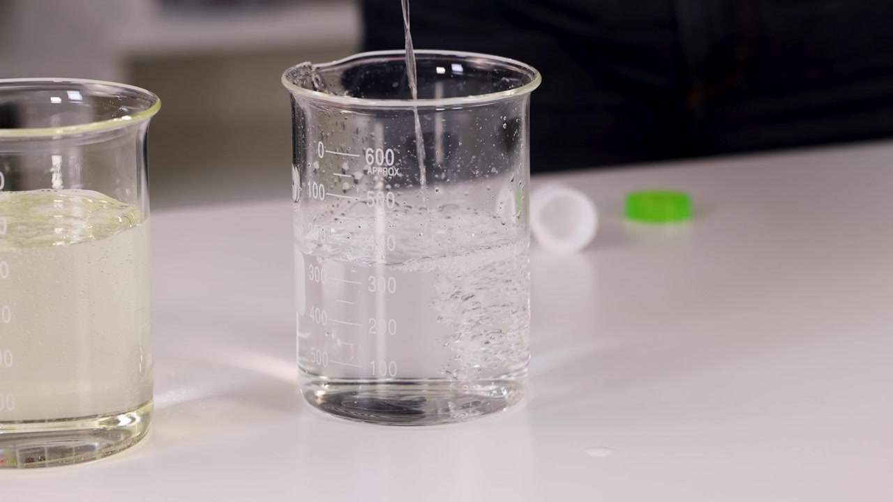 Primo piano di liquido trasparente che si versa in un becher di vetro durante un esperimento di chimica in laboratorio