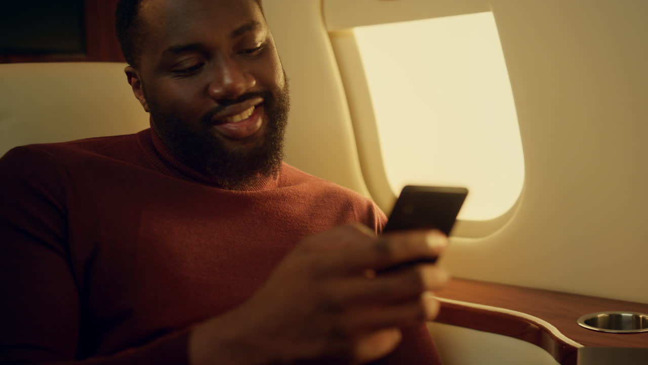 un tipo positivo chateando en línea en un viaje en avión. las manos sosteniendo un primer plano de teléfono inteligente.