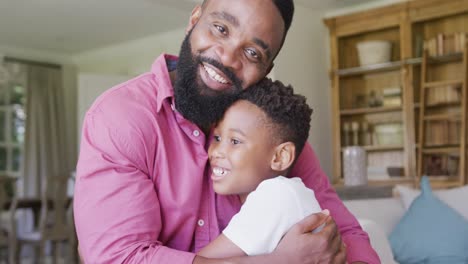 Portrait-of-happy-african-american-father-and-son-sitting-on-sofa-and-embracing,-in-slow-motion