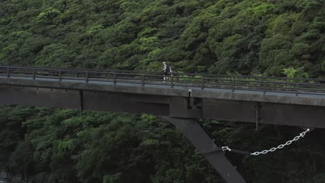 Man-walking-across-bridge,-forest-in-background,-tracking-shot,-Yakushima-Japan