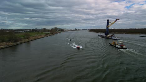 two speedboats moving past the container ships that are moving construcion cranes and materials over de canal in the netherlands