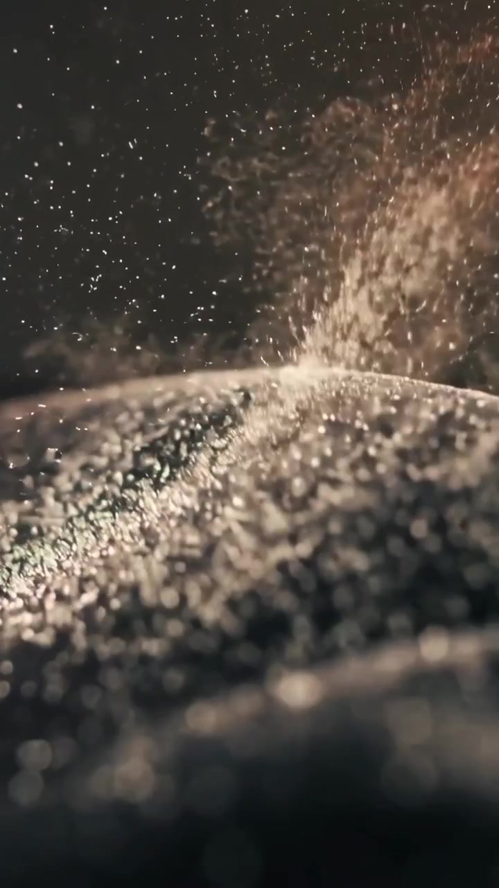 Video verticale: Particelle in caduta che reagiscono a un impulso d'aria fuori campo, sollevandosi su una superficie granulosa retroilluminata