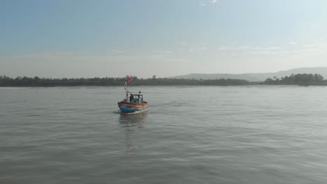 tiro de dron de un pequeño y colorido barco de pesca indio que sale al mar mirando hacia la orilla