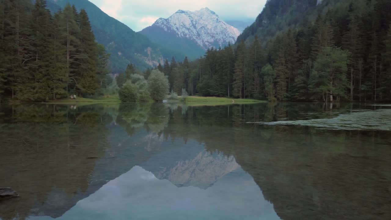 Alpine mountain range reflecting in lake Plansar or Plansarsko jezero in Jezersko, Slovenia in autumn, fast pan left to right
