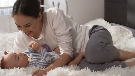 Loving-Mom-Lying-On-Fluffy-White-Bedspread-In-Bedroom-With-Her-Baby,-Gently-Stroking-His-Head-And-Kissing-Him