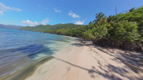 Speed-FPV-flight-over-Sandy-beach,-along-Caribbean-sea-with-coral-reef-and-palm-trees-in-summer