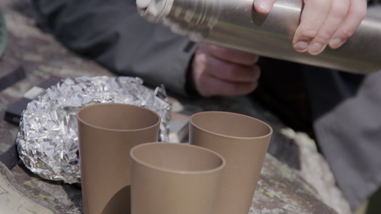 Coffee being served from a thermos into cups on a rock during a forest hike. Proper outdoor luxury.