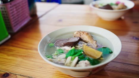 A-full-bowl-of-hot-delicious-Thai-chicken-soup-with-rice-noodles,-sprouts-and-greens-in-an-outdoor-street-food-cafe