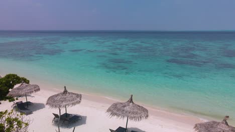 Drone-flight-over-the-beach-with-palm-umbrellas-towards-the-turquoise-water-of-the-ocean