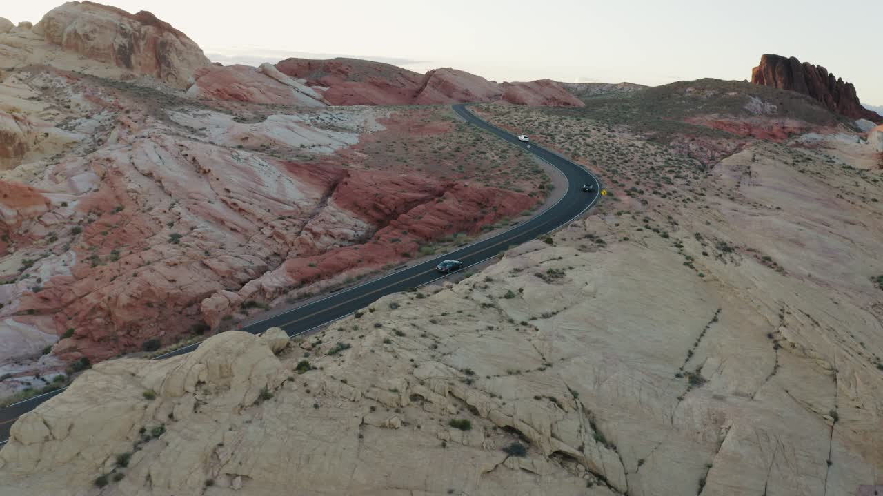 автомобили, проезжающие по холмам и каньонам долины огня на закате в неваде