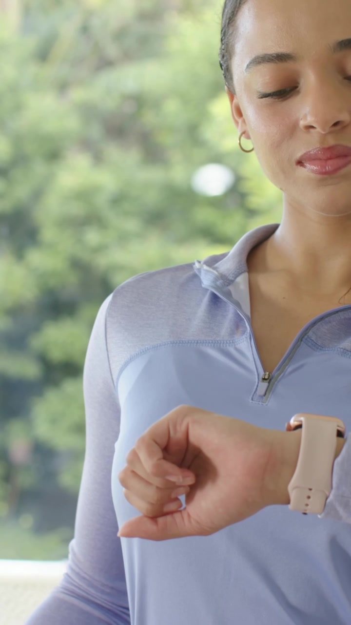 Vertical video: Glancing woman in zip top tapping smartwatch on patio, checking time, copy space