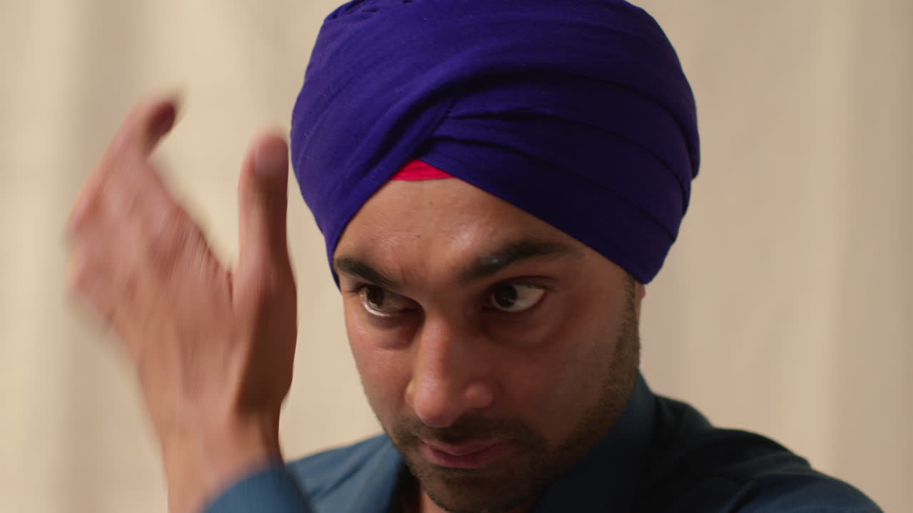 fotografía de estudio de un hombre sikh usando y comprobando un turbante contra un fondo plano