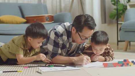 플라스틱 장난감 벽돌로 방 바닥에 누워있는 아시아 아버지와 아들의 클로즈업 스마트 폰을보고 집에서 함께 그림을 그리고 있습니다.
