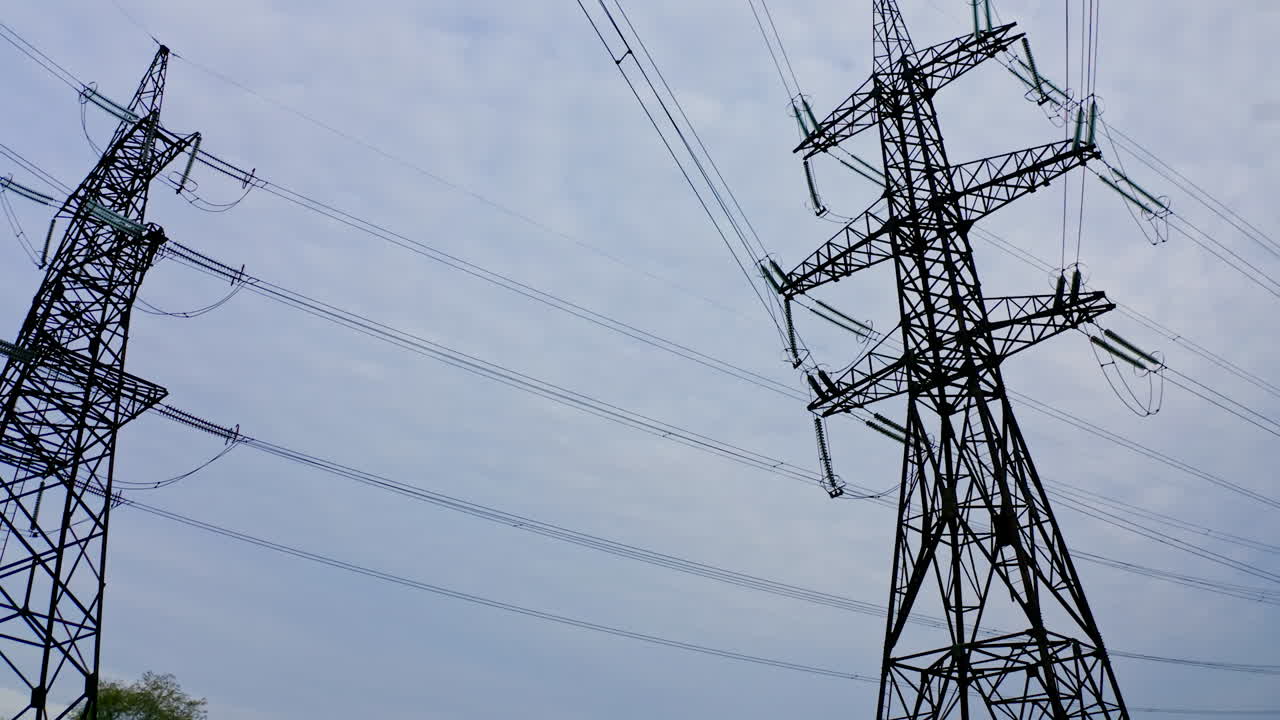 High electric towers with wires. Power transmission pylons under the light sky. Electricity distribution station. View from below.