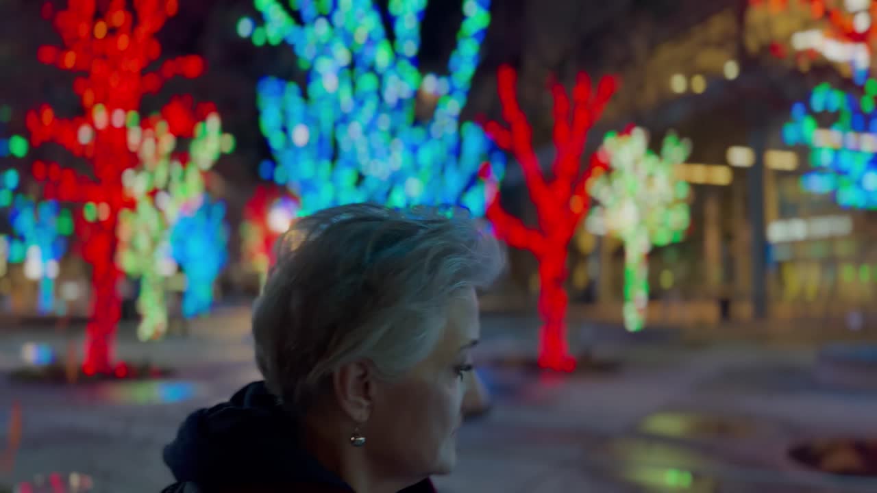 mujer mayor caminando en una ciudad decorada con luces de navidad por la noche