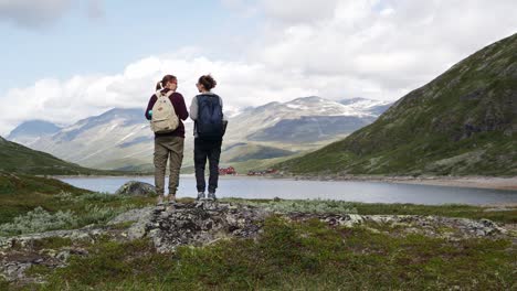 two women backpackers standing in front of a mountain lake and enjoying the view