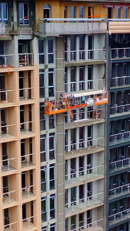 high-rise architecture under construction. workers on the outdoor lift doing the beautiful facade of multi-storey building. vertical video