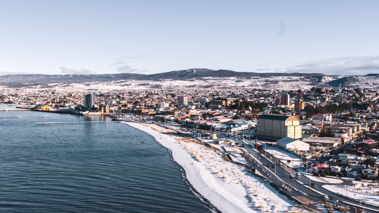 Hyperlapse zoom in aerial view of Punta Arenas coastline in Chile, with snow covering the city and shore
