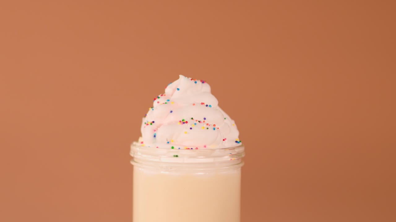 Human hand decorates vanilla milkshake with cookie and striped straw against warm studio background