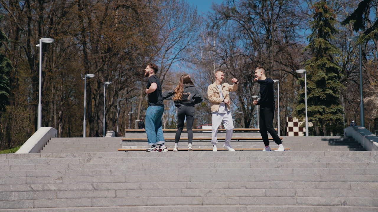 Funny young people dancing outdoors. Group of guys and a girl having joy together in the city park in sunny autumn day. Happy friendship.