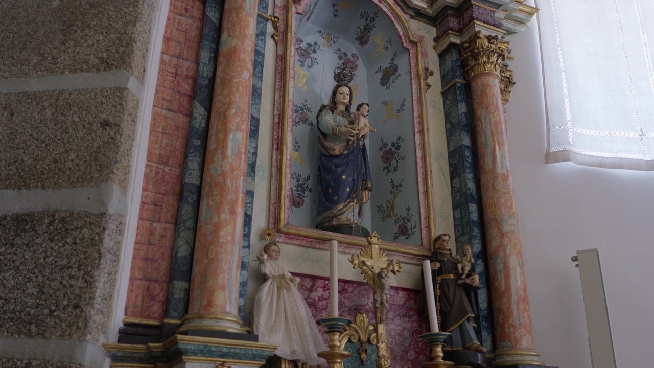 Socha Madony držící Ježíška uvnitř květinově malovaného výklenku kostelního oltáře.