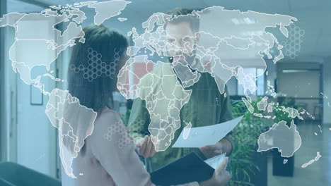 male colleague and female colleague discussing reports in business office showing world map overlay