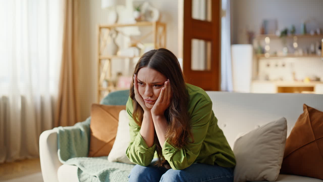 Exhausted woman sitting home sofa closeup. Sad young brunette touching head
