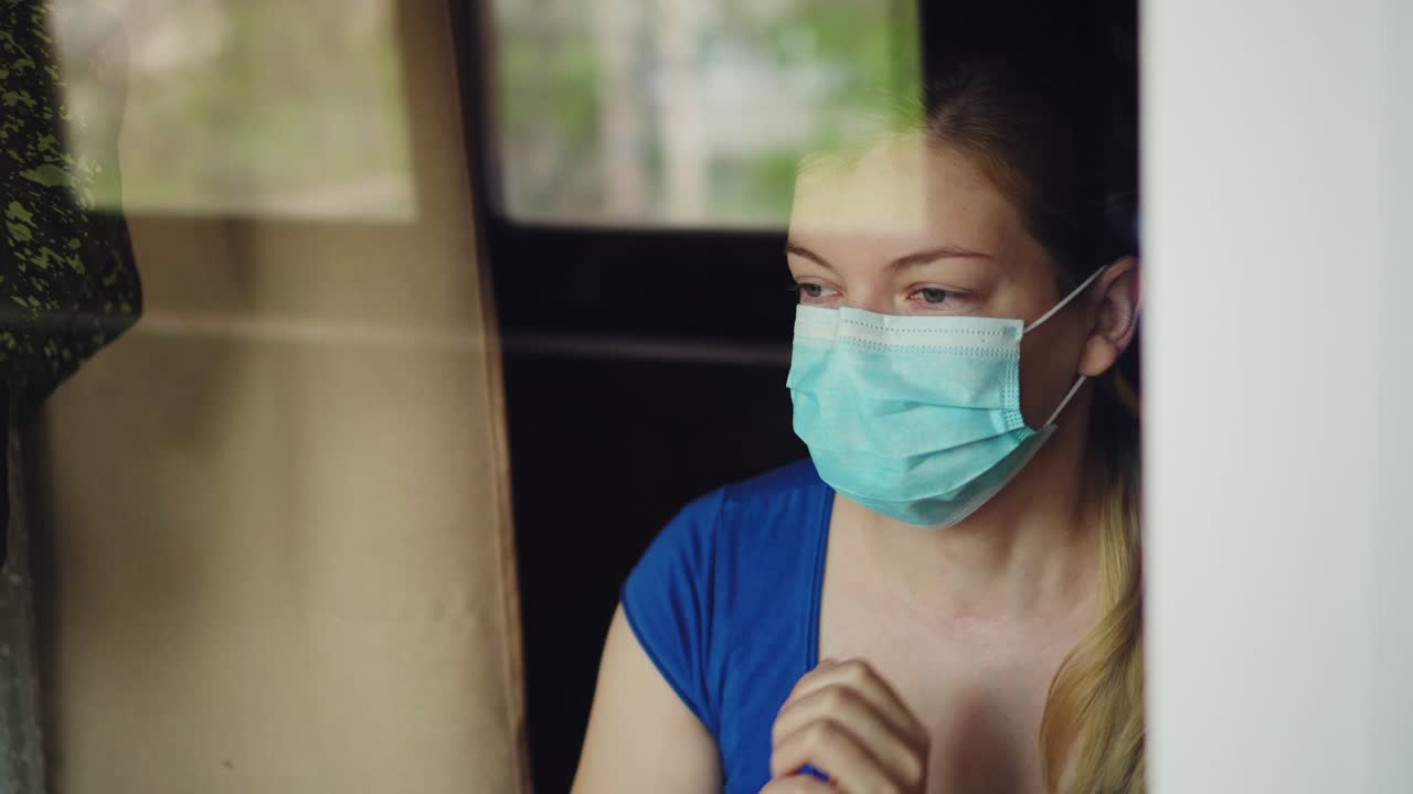 una mujer con una máscara médica mira por la ventana y habla en el móvil 01