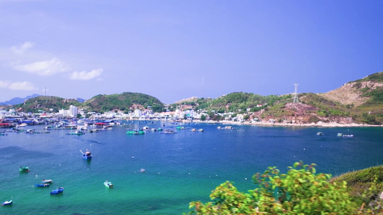Det klare vannet i Ninh Thuan i Vietnam. Båter beveger seg inn og ut av havnen mens solen skinner sterkt over. Kystlandskapet er synlig i bakgrunnen.