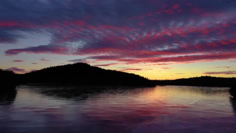 Aerial-footage-flying-low-across-the-surface-of-a-frozen-pond-through-a-straight-and-towards-a-colorful-sunrise