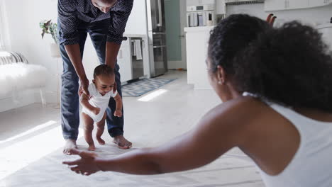 parents encouraging smiling baby son to take first steps and walk at home
