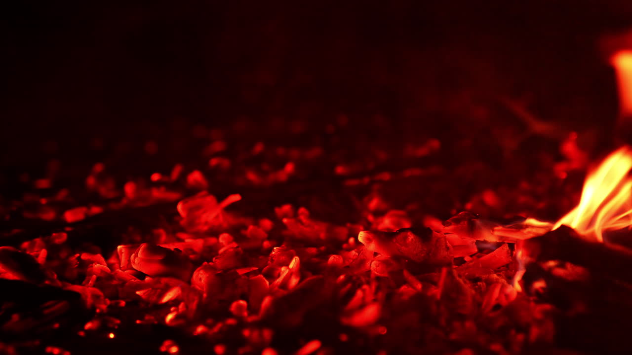 Glowing pieces of charcoal sparkling beautifully. Little flames of fire break out again. Close up.