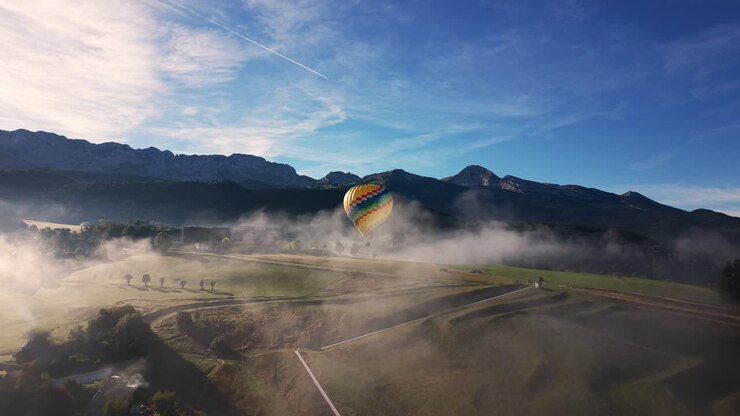 Hot air balloon drifting through morning fog over a rural valley in Auvergne Rhone Alpes. Aerial, Push Forward Shot