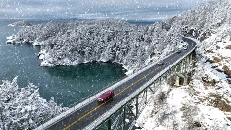 cars driving across deception pass bridge with snow falling and covering the ground