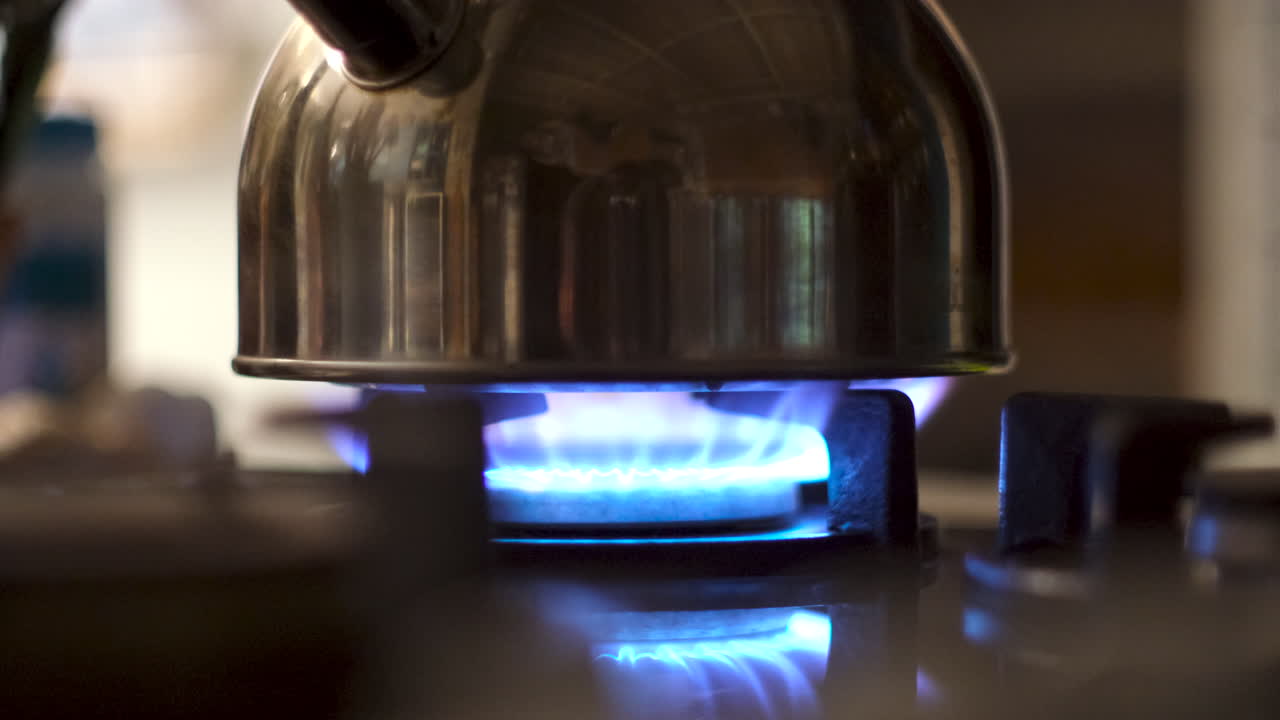 Low angle closeup of blue flame from gas stove burner heating water in kettle